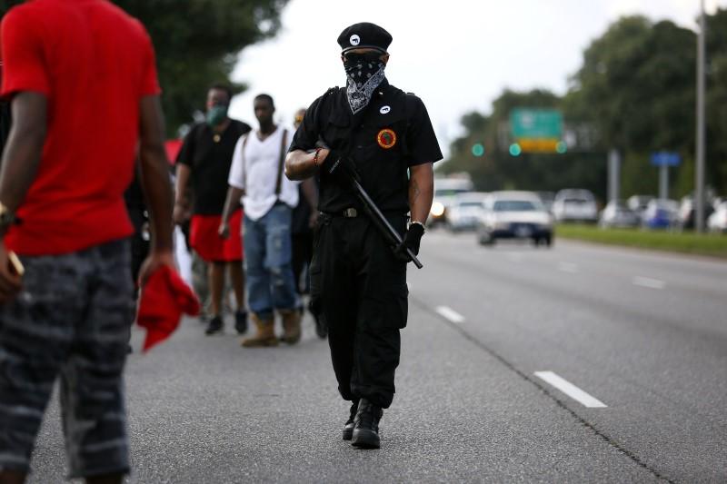 A demonstrator wearing the insignia of the New Black Panthers Party carries a shotgun during a protest against the shooting death of Alton Sterling , near the headquarters of the Baton Rouge Police Department in Baton Rouge, Louisiana, U.S. July 9, 2016.  REUTERS/Jonathan Bachman